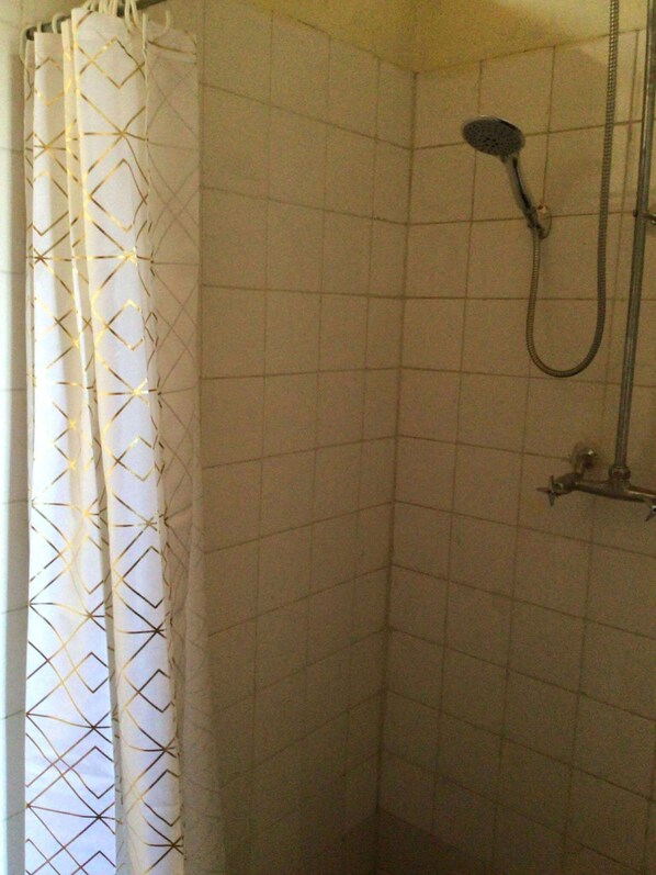 Zona de ducha con ducha, manguera, paredes de azulejos y cortina estampada.