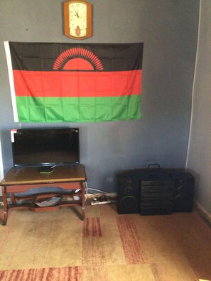 A room with a flag, a clock, a table with a laptop, and a speaker.