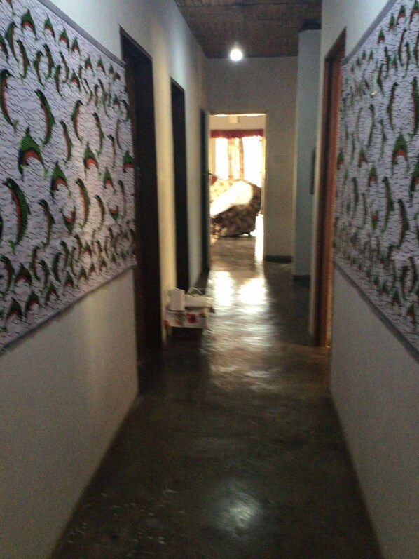 A narrow hallway with patterned wallpaper on the walls, leading to a room with a bed and a window.