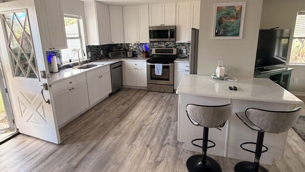 A modern kitchen with white cabinets, a central island with stools, a microwave, oven, and a sink. - 2-bedroom house in the villages with golf course view and included golf cart! (Lady Lake)