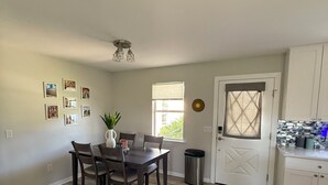 A dining area with a table and chairs, a window with blinds, a door with a geometric design, and a trash can. - 2-bedroom house in the villages with golf course view and included golf cart! (Lady Lake)