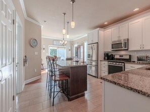 A modern kitchen with white cabinets, stainless steel appliances, and a central island with bar stools. - Steps to the Beach. 4 Bedrooms. Occupancy 10 (Town Bank)