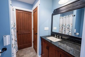A bathroom with a wooden door, a sink with a mirror, and a shower curtain. - The Lookout at Buckleberry View, EV Charging (Spring Mills)