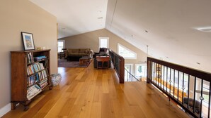 A spacious loft with a high ceiling, wooden flooring, a bookshelf, a sofa, and a view through large windows. - The Lookout at Buckleberry View, EV Charging (Spring Mills)