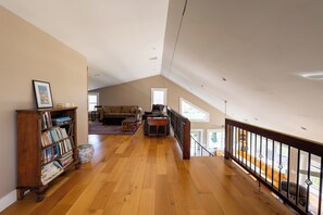 A spacious loft with a high ceiling, wooden flooring, a bookshelf, a sofa, and a view through large windows. - The Lookout at Buckleberry View, EV Charging (Spring Mills)