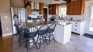A kitchen with a central island, bar stools, wooden cabinets, stainless steel appliances, and pendant lighting. - The Lookout at Buckleberry View, EV Charging (Spring Mills)