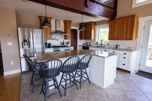 A kitchen with a central island, bar stools, wooden cabinets, stainless steel appliances, and pendant lighting. - The Lookout at Buckleberry View, EV Charging (Spring Mills)