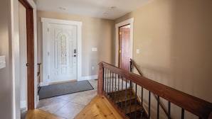 A hallway with a wooden staircase, a white door with a stained glass window, and beige walls. - The Lookout at Buckleberry View, EV Charging (Spring Mills)
