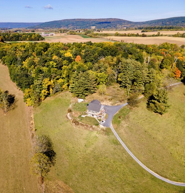 An aerial view of a rural property with a large house surrounded by dense forest, a winding road, and open fields. - The Lookout at Buckleberry View, EV Charging (Spring Mills)