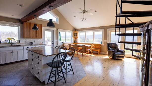 A spacious kitchen with a large island, wooden cabinets, and a dining area with chairs. - The Lookout at Buckleberry View, EV Charging (Spring Mills)