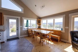 A spacious kitchen with a large wooden table, built-in bench seating, and large windows offering a view of the outdoors. - The Lookout at Buckleberry View, EV Charging (Spring Mills)