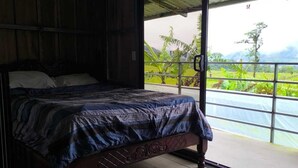 Un dormitorio con cama, paredes de madera y vistas a un paisaje verde a través de una puerta corredera.
