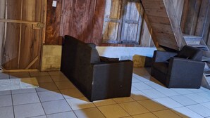 Un cuarto rústico en el ático con vigas de madera, un techo inclinado y un ventanal grande. Hay dos sofás negros y una mesita.