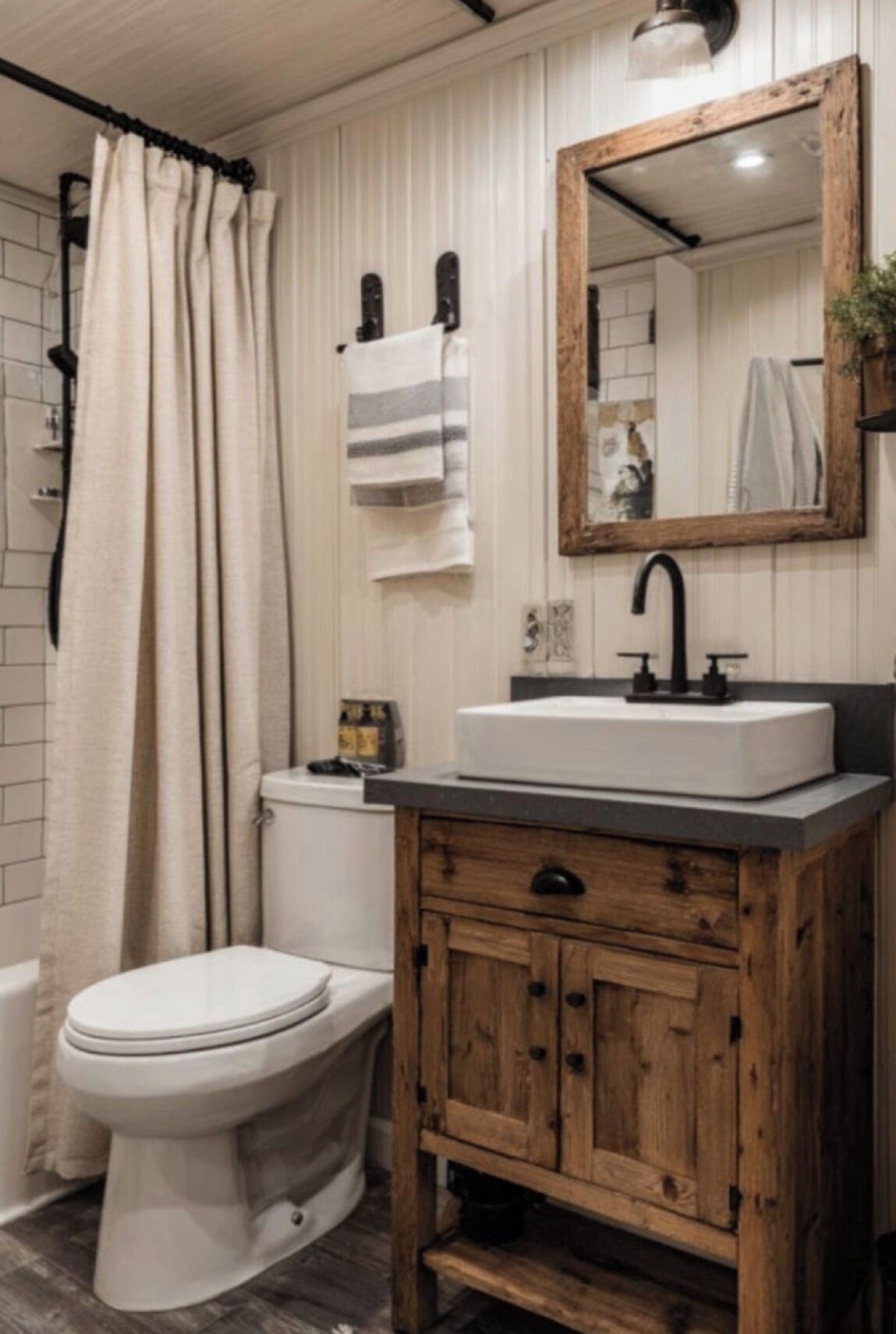 Une salle de bain avec des toilettes blanches, un meuble-lavabo en bois avec un miroir et un rideau de douche.