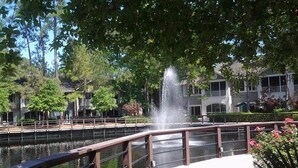 A bridge with a water fountain, surrounded by trees and a building with a white facade. - Island Links - 3BR/2BA - Great Pool Complex! (Hilton Head Island)