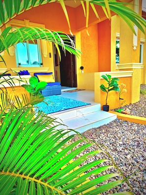 A house with a tiled patio, a blue mat, and a small garden area with pebbles and plants.
