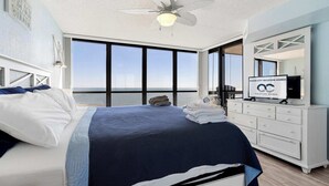 A bedroom with a bed, a ceiling fan, a dresser, and a large window with a view of the ocean. - Golden Sands 1407 (Ocean City)