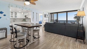 A modern living space with a dining area, kitchen, and a large window offering a view. - Golden Sands 1407 (Ocean City)