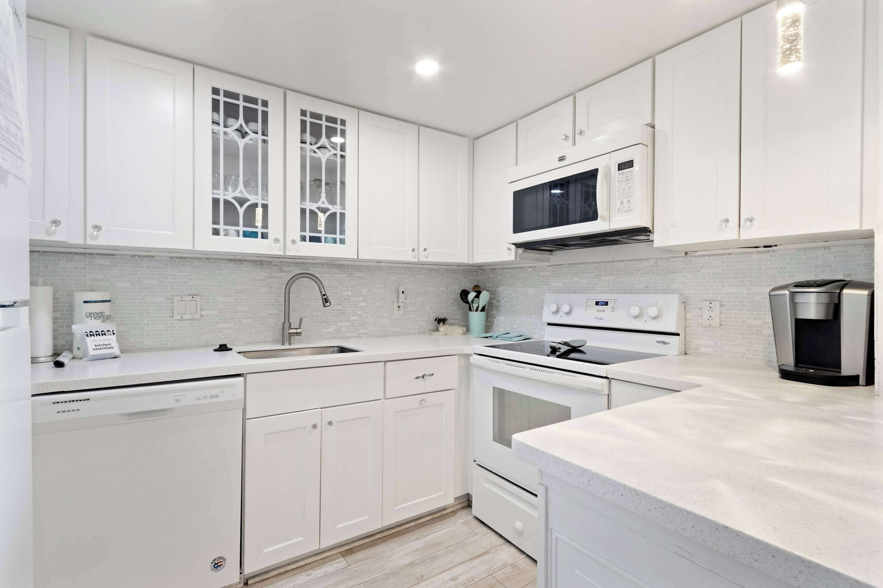 A modern kitchen with white cabinetry, a built-in microwave, a dishwasher, and a coffee maker.