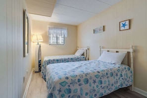 Une chambre avec deux lits, une fenêtre avec un rideau blanc, une décoration en forme d’étoile fixée au mur et un petit cadre photo.