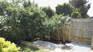 A backyard with a wooden fence, a gravel path, and various plants. - Abe’s Home (London)