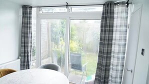 A room with a large sliding glass door leading to a garden. - Abe’s Home (London)
