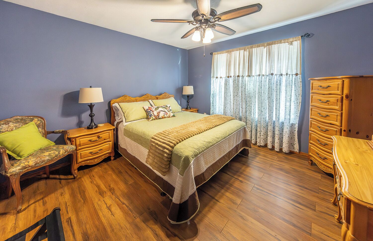 A bedroom with a bed, nightstands, a dresser, and a ceiling fan.