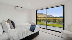 A bedroom with a large window, a bed with pillows, and a chair. - Rubus Street Residence | Brand-New 4 Bedroom, 4 Bathroom Retreat in Wanaka (Wanaka)