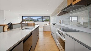 A modern kitchen with a large island, built-in appliances, and a view of the mountains through the windows. - Rubus Street Residence | Brand-New 4 Bedroom, 4 Bathroom Retreat in Wanaka (Wanaka)