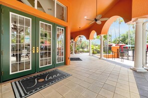 Entrada de un hotel con una puerta verde, felpudo que dice 'Savana' y un patio con baldosas y mobiliario exterior.