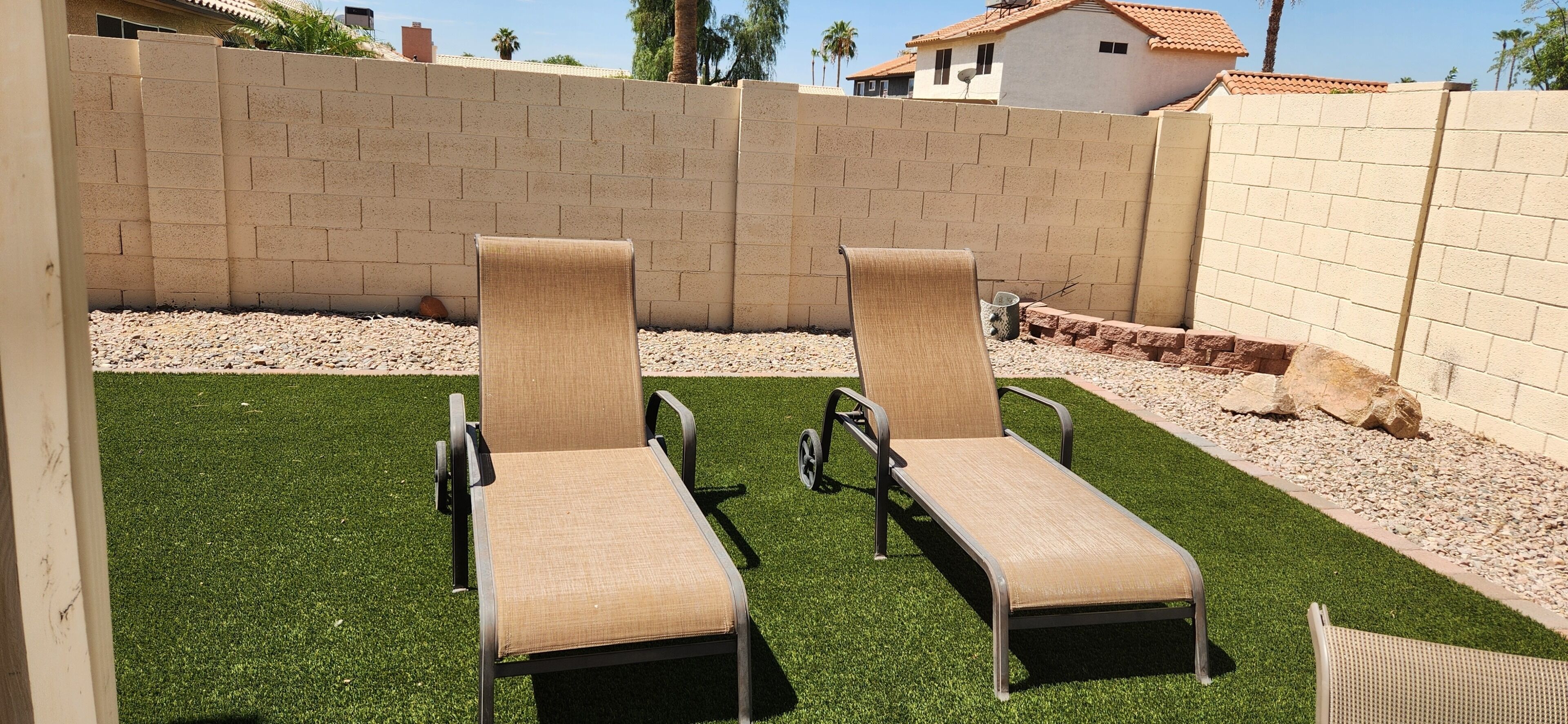 Two lounge chairs on artificial grass, a brick wall, and a small rock garden.