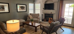 A living room with a sofa, armchair, coffee table, lamp, guitar, fireplace, and framed artwork on the wall. - 4-bedroom house with a heated pool in northern Phoenix (Phoenix)