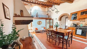 Un coin repas chaleureux avec une table et des chaises en bois, une cuisine agrémentée d’éléments en pierre et un balcon doté d’une balustrade.