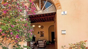Une entrée avec un sol carrelé, une porte en bois et un pot de fleurs contenant des fleurs roses.