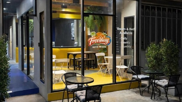 A modern cafe with outdoor seating, a neon sign, and a glass facade. - Free Way Kata Beach Hostel (Karon)
