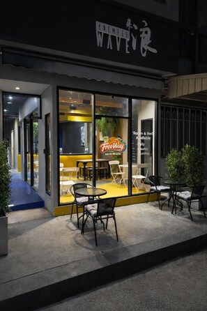 A modern cafe with outdoor seating, a neon sign, and a glass facade. - Free Way Kata Beach Hostel (Karon)