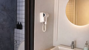 A bathroom with a toilet, a sink, a mirror, and a hairdryer on the wall. - Free Way Kata Beach Hostel (Karon)