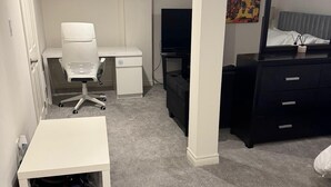 A bedroom with a white desk, a chair, a TV, a dresser, and a bed.