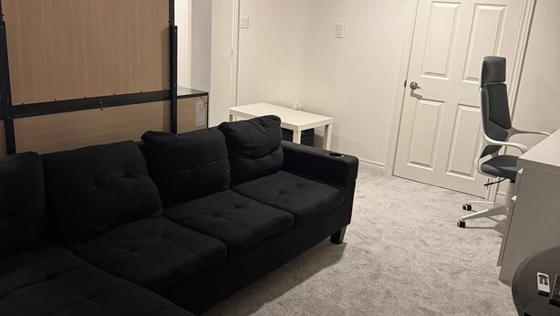 A modern living room with a sectional sofa, a small white table, a black office chair, and a closed door.