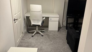 A small, clean room with a white desk, a chair, a TV, and a door.