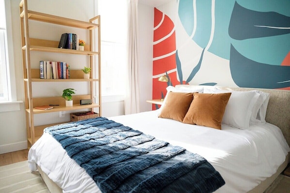 A bedroom with a bed, a bookshelf, and a wall with abstract art.