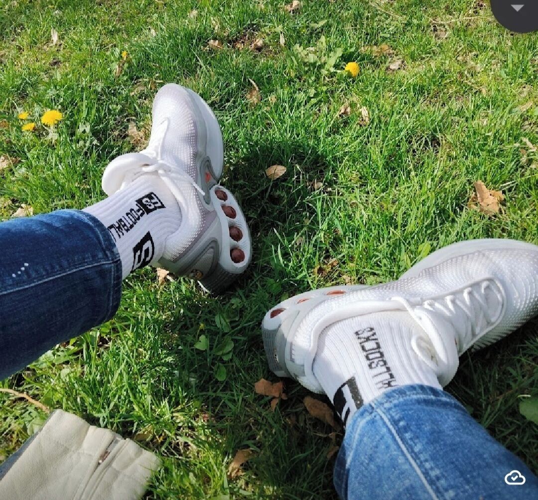 A pair of white sports shoes with red accents on grass.