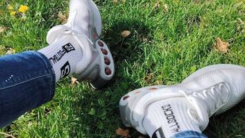 A pair of white sports shoes with red accents on grass.