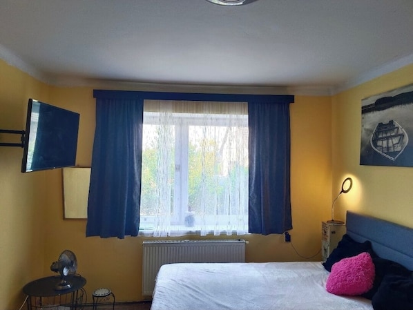 Une chambre d’hôtel comprenant un lit, un bureau avec une chaise, une fenêtre avec des rideaux, un téléviseur fixé au mur et un tableau.