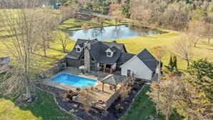 Une grande maison avec une piscine, un étang et une pelouse bien entretenue.