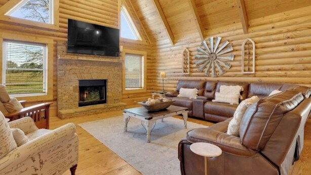 L’intérieur d’une cabane en rondins, avec une cheminée en pierre, des canapés en cuir et un téléviseur fixé au mur.