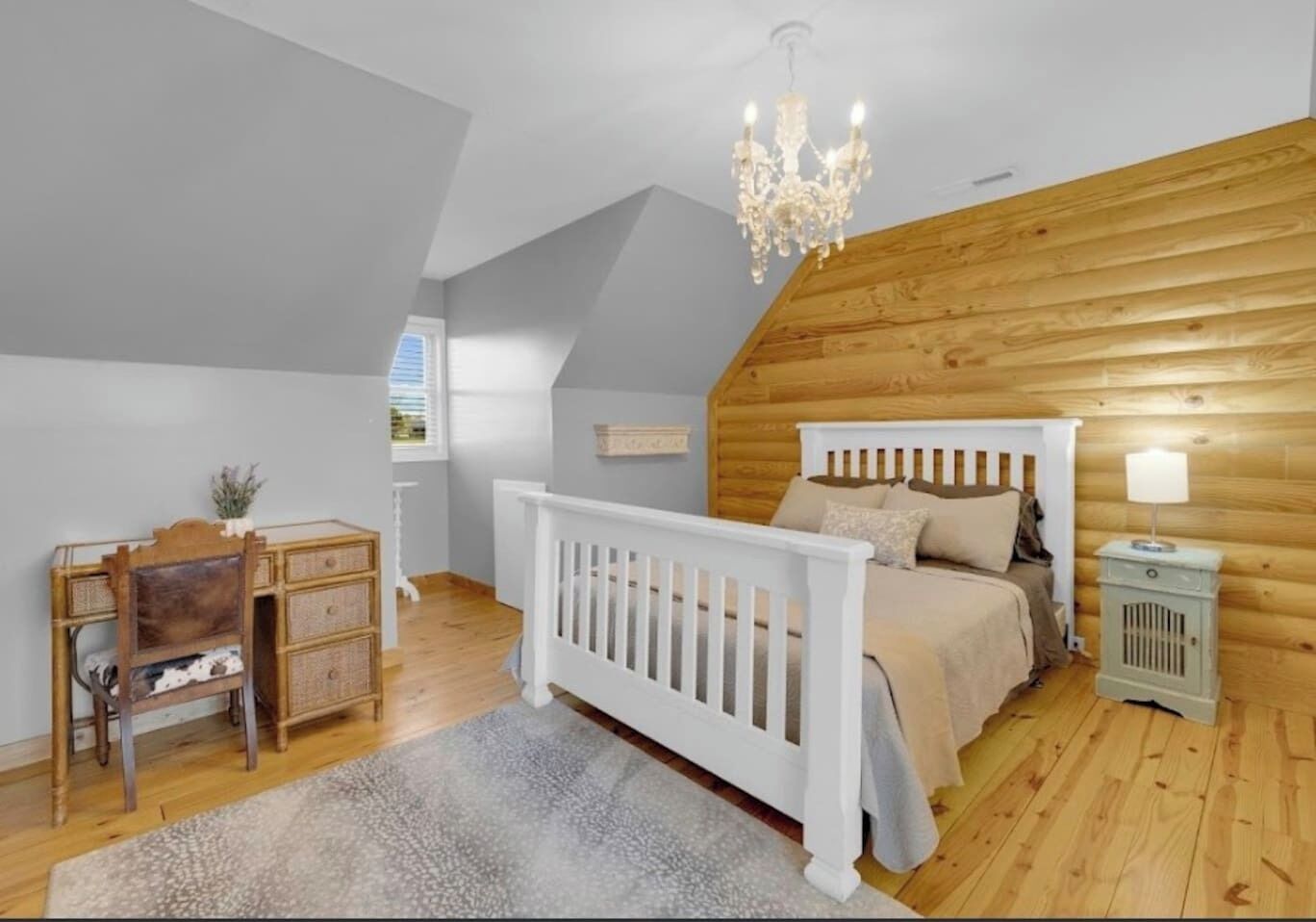 Een slaapkamer met schuine plafonds, houten wanden, een wit ledikant, een houten bureau en een kroonluchter.