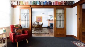 Una sala de estar acogedora con un sillón rojo, una mesa de comedor con sillas y una estantería llena de libros.