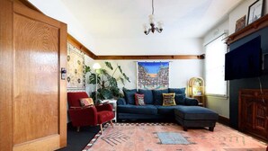 Un salón acogedor con un sofá modular, un sillón rojo, una planta grande y una alfombra colorida.