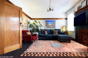 A cozy living room with a sectional sofa, a red armchair, a large plant, and a colorful rug. - Art Deco Home - Walk to Manubread and Star Cinema (Invermay)